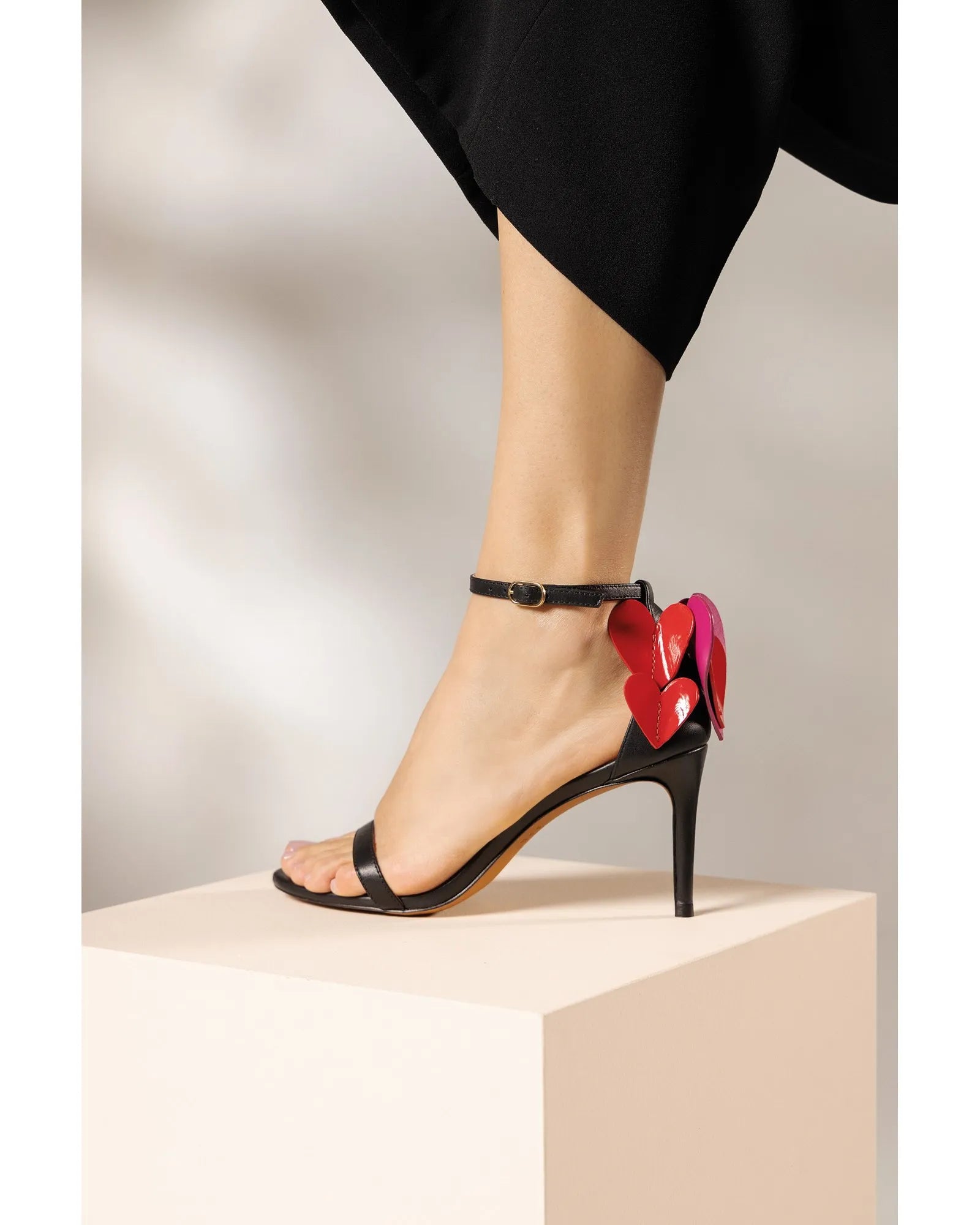 Black high-heeled sandal with a colorful flower detail on a neutral background